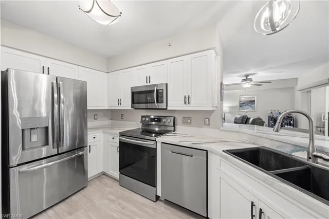 a kitchen with stainless steel appliances granite countertop a refrigerator stove a sink dishwasher and white cabinets with wooden floor