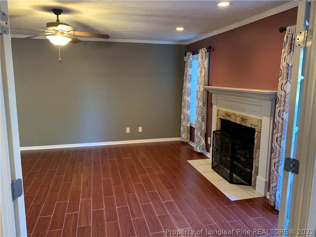 5428 Arnette Road Hope Mills, NC 28348 - Photo 9 of 41 an empty room with wooden floor a fireplace a ceiling fan and staircase