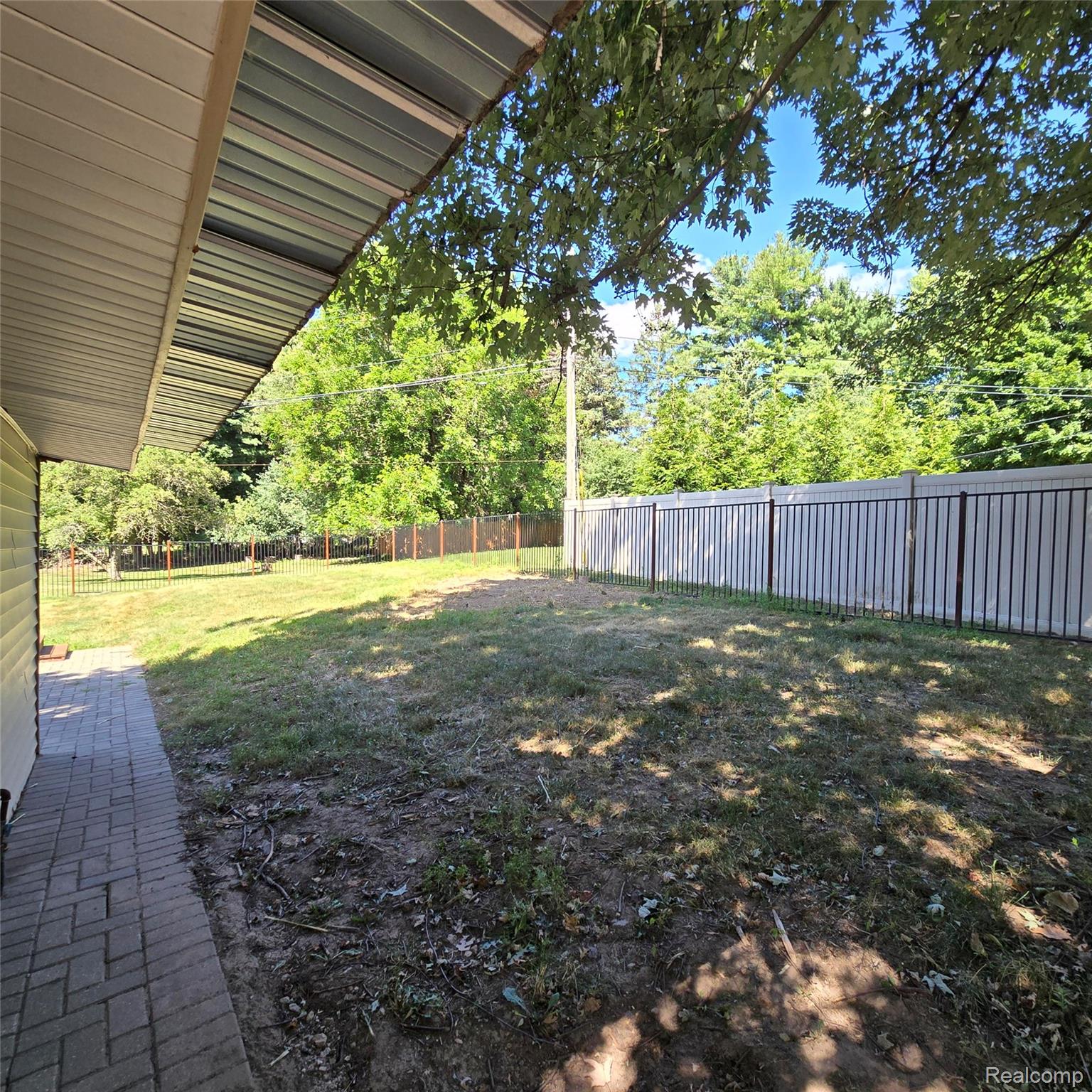 311 Nevada Avenue Rochester, MI 48309 - Photo 54 of 70 Expansive backyard featuring a partial privacy fence, mature trees, a covered patio area with a metal roof, and a paver stone walkway