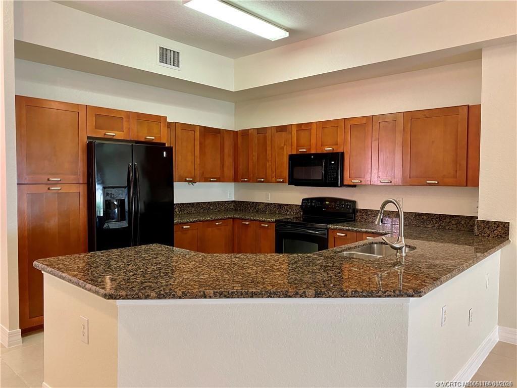 59 Southeast Palermo, Unit 102 Stuart, FL 34994 - Photo 4 of 18 a kitchen with granite countertop wooden cabinets a refrigerator and a sink