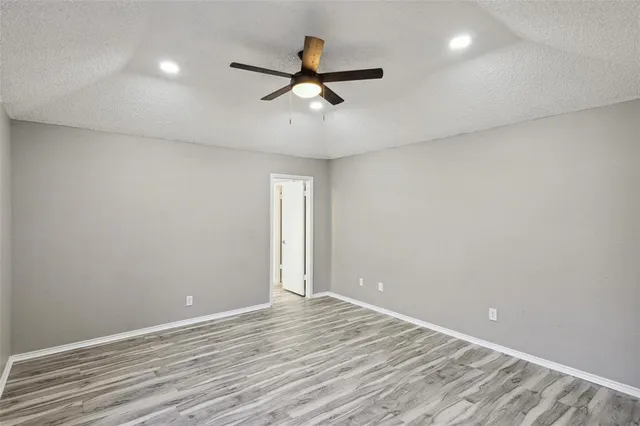 an empty room with wooden floor ceiling fan and windows