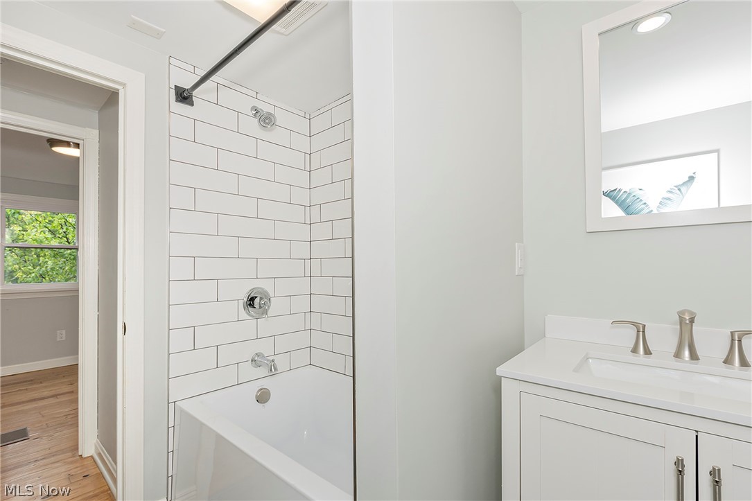 3719 Walter Road North Olmsted, OH 44070 - Photo 29 of 35 Bathroom featuring a white subway tile tub surround, white vanity with integrated sink, brushed nickel faucet, and a framed mirror