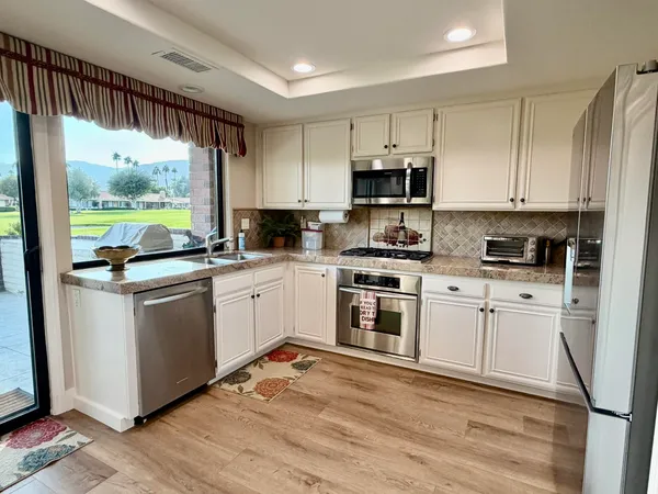 a kitchen with white cabinets appliances a sink and a window