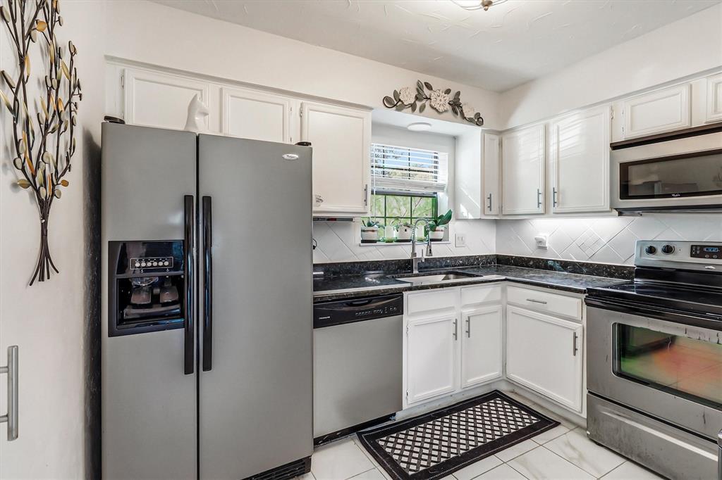 15151 Berry Trail, Unit 1307 Dallas, TX 75248 - Photo 9 of 27 Kitchen with stainless steel appliances, white cabinets, tasteful backsplash, and dark stone counters