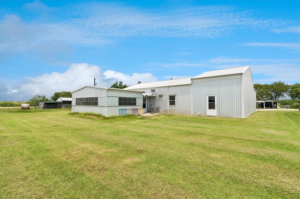 3007 McReynolds Road Sanger, TX 76266 - Photo 33 of 39 Corrugated metal siding structure with a broad lawn, two single entry doors, multiple window units, and an attached covered carport