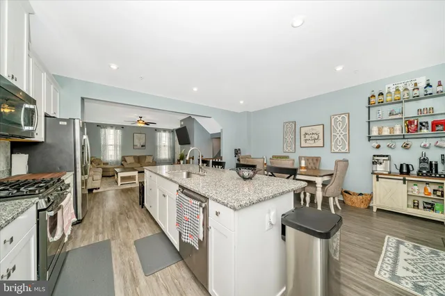 a kitchen with stainless steel appliances granite countertop a stove top oven a sink a dining table and chairs with wooden floor