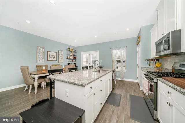 a large white kitchen with stainless steel appliances granite countertop a stove and a dining table chair
