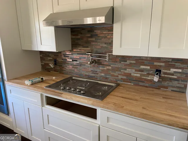a kitchen with granite countertop a stove a sink and white cabinets