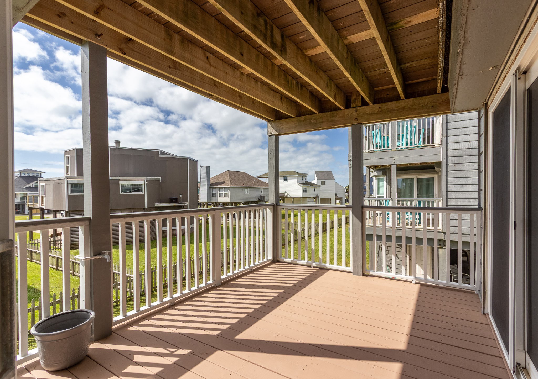 17609 Termini-San Luis Pass Road Galveston, TX 77554 - Photo 25 of 37 A cozy wooden deck with white railings, offering a view of neighboring houses and a grassy yard. Ideal for relaxation or entertaining, with partial shade from the overhead structure.