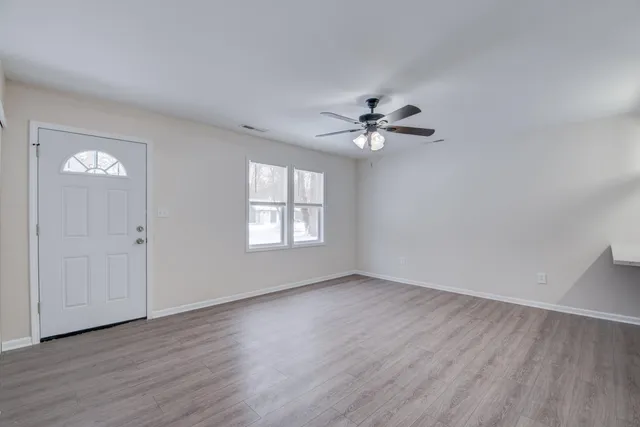 an empty room with wooden floor chandelier fan and windows