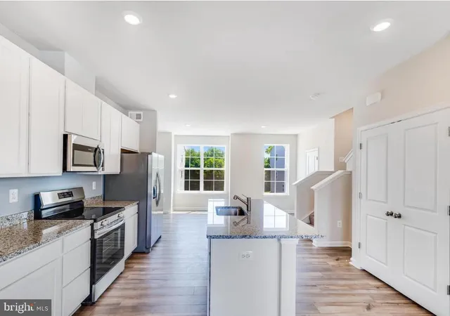 a kitchen with granite countertop a refrigerator a stove top oven a sink dishwasher and white cabinets with wooden floor