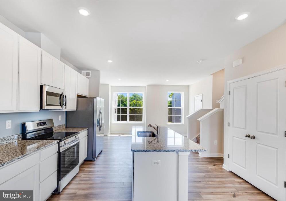 a kitchen with granite countertop a refrigerator a stove top oven a sink dishwasher and white cabinets with wooden floor