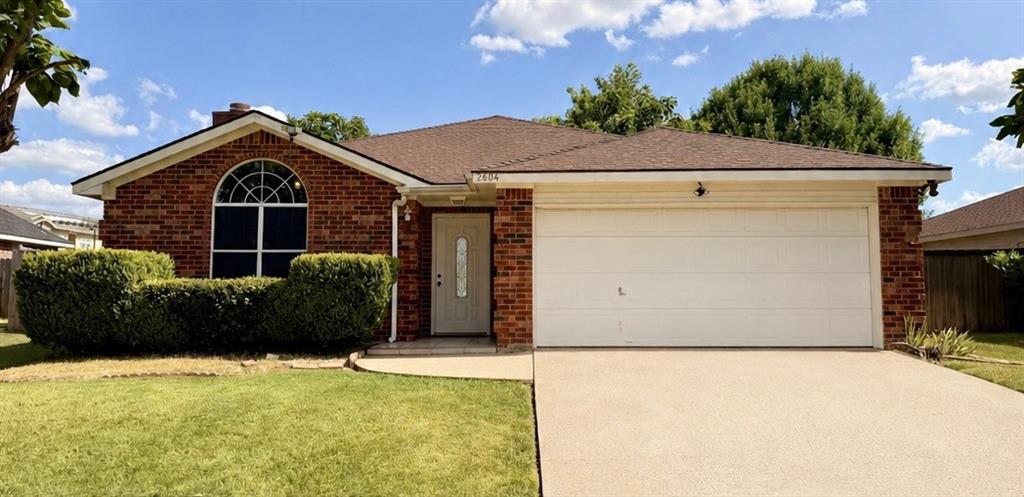 2604 Crix Lane Fort Worth, TX 76140 - Photo 1 of 13 Brick facade residence featuring a two-car garage, an arched window, a front door with decorative glass inserts, a shingled roof, and green shrubbery