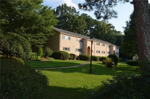 a view of a white house in front of a big yard with plants and large trees