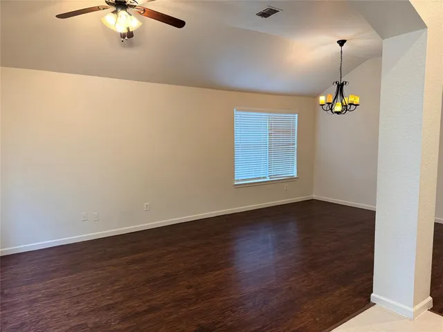 an empty room with wooden floor chandelier fan and windows