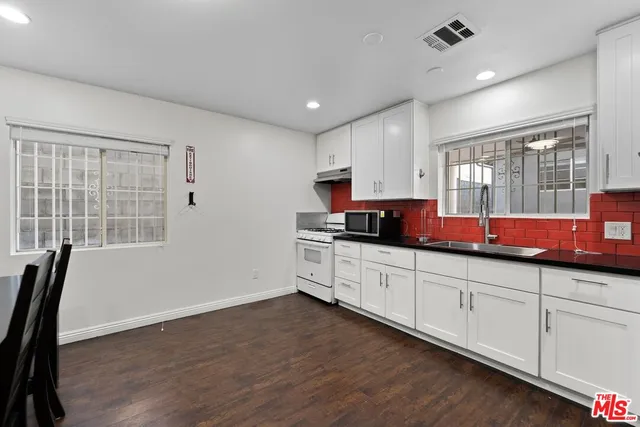 a kitchen with granite countertop a stove top oven a sink dishwasher a dining table and chairs with wooden floor