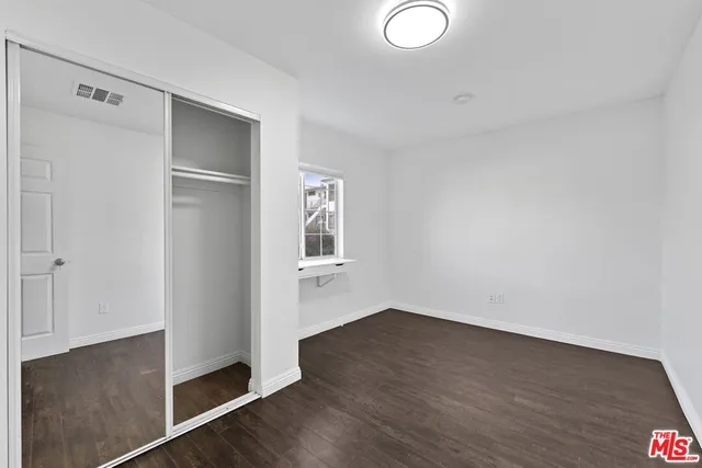 a view of an empty room with wooden floor and closet
