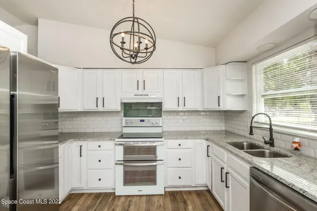 a kitchen with stainless steel appliances granite countertop a refrigerator a stove a sink and white cabinets