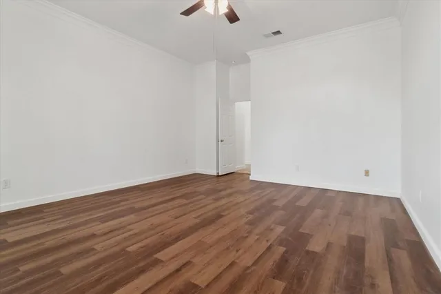 a view of an empty room with wooden floor a ceiling fan and window