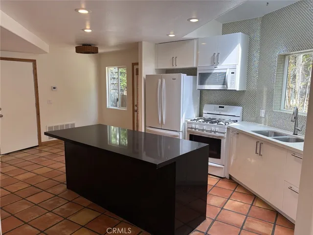 a kitchen with stainless steel appliances granite countertop a refrigerator a sink dishwasher a stove and white countertops with wooden floor