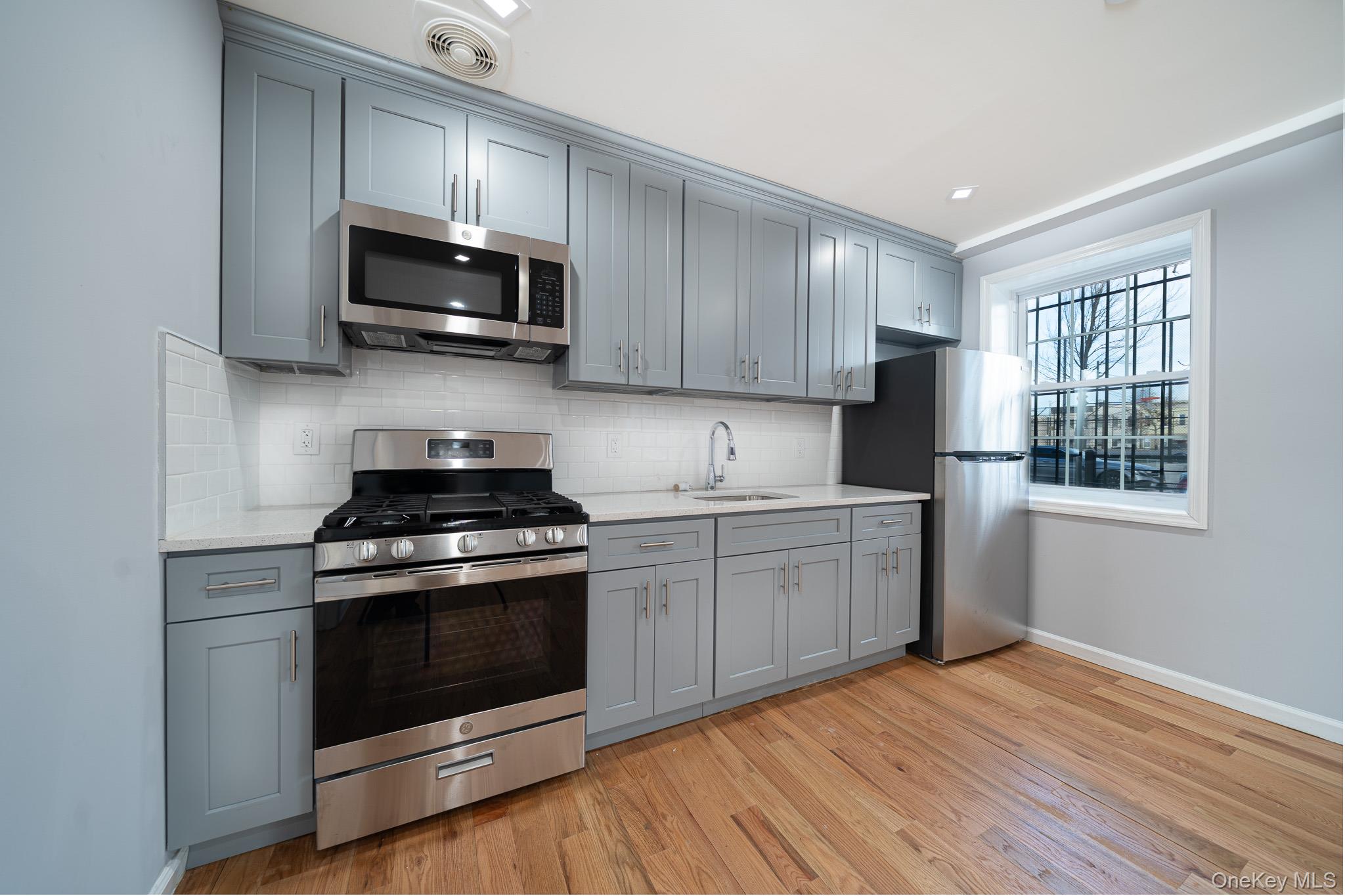 70-36 70th Street Queens, NY 11385 - Photo 4 of 29 Kitchen featuring appliances with stainless steel finishes, gray cabinetry, decorative backsplash, and light stone countertops