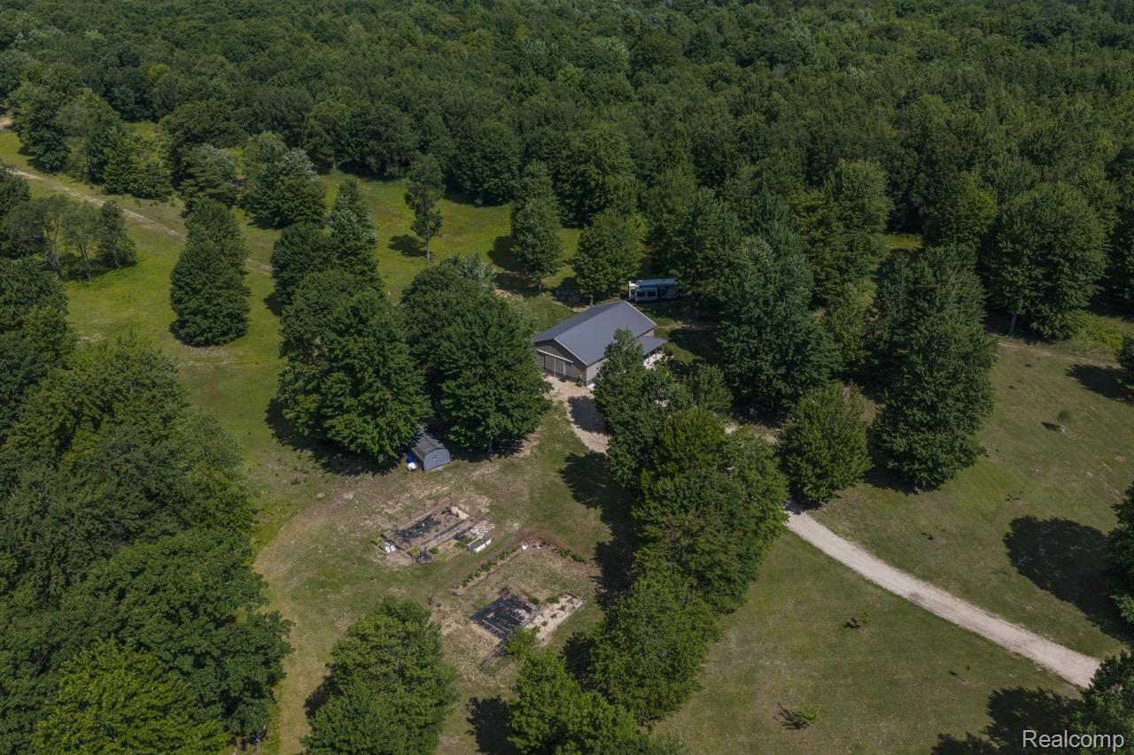 2418 South 41st Road South Cadillac, MI 49601 - Photo 36 of 57 Aerial perspective showcasing a single-story residence with a dark-pitched roof, surrounded by extensive mature trees and verdant landscaping