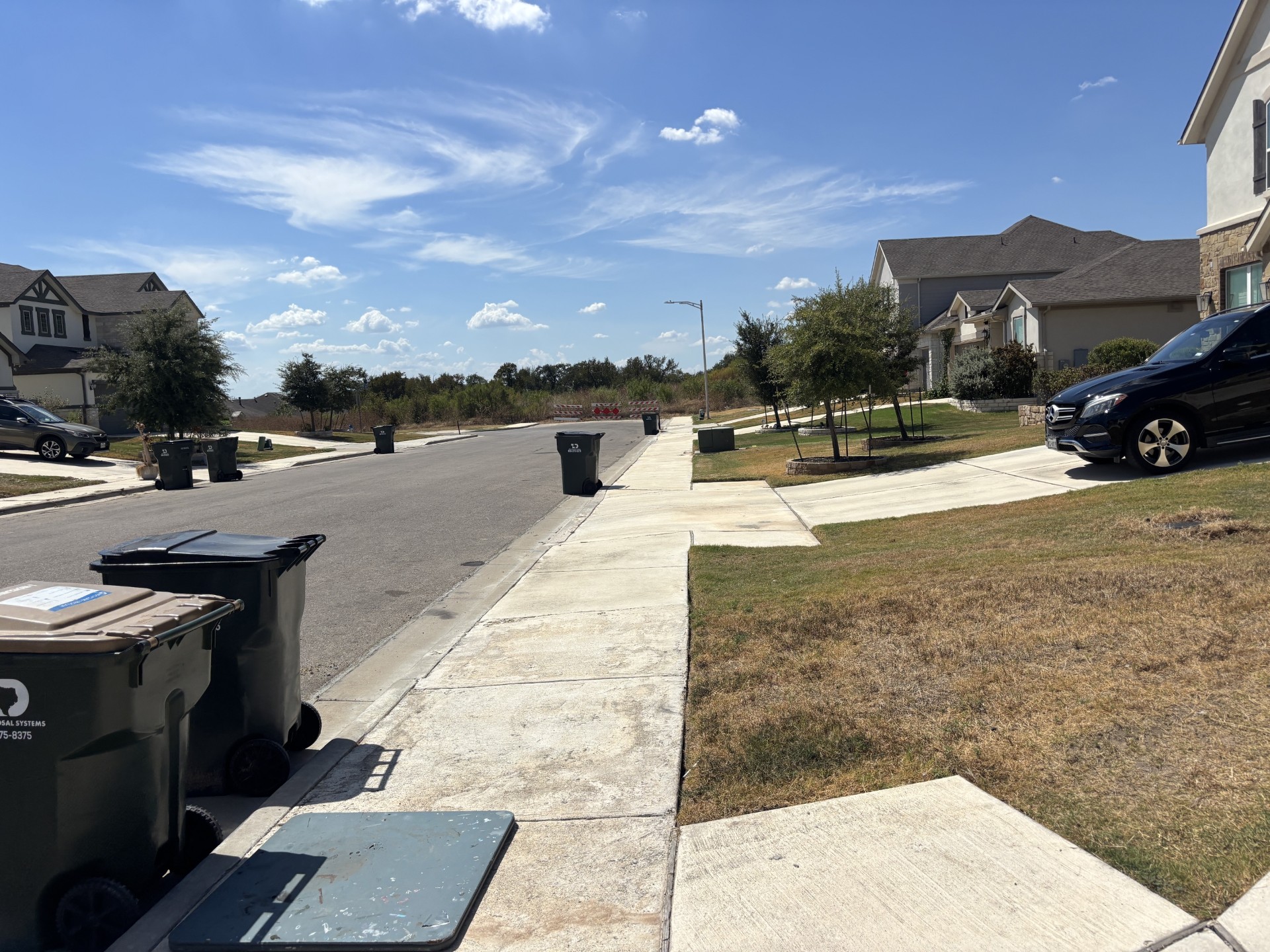2000 Chamberlin Trail Georgetown, TX 78626 - Photo 10 of 12 Concrete sidewalks line the quiet suburban neighborhood street under a bright blue sky.