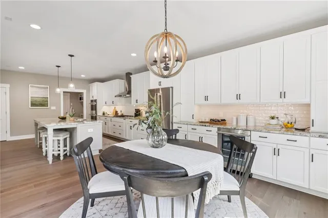 a kitchen with stainless steel appliances granite countertop a dining table chairs stove and white cabinets