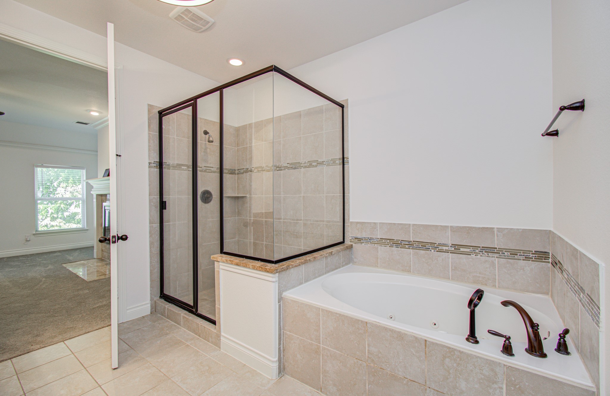 6621 North Main Street Houston, TX 77009 - Photo 17 of 41 Ensuite bathroom features a spacious walk-in shower with glass doors and a tiled surround, alongside a large corner bathtub. Neutral tile flooring and walls create a clean, modern look, and the room opens into a connected carpeted area with a window and fireplace.