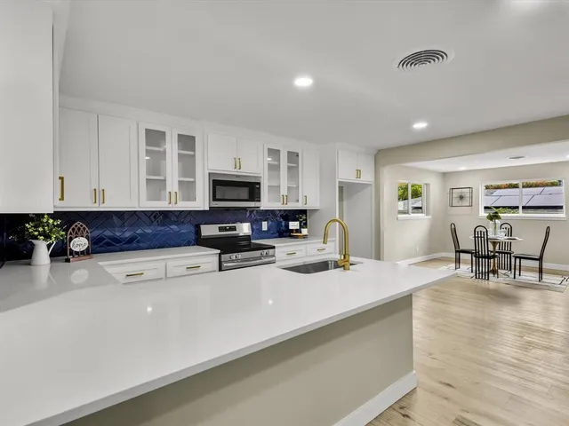 a kitchen with stainless steel appliances granite countertop a stove top oven a sink a dining table and chairs with wooden floor