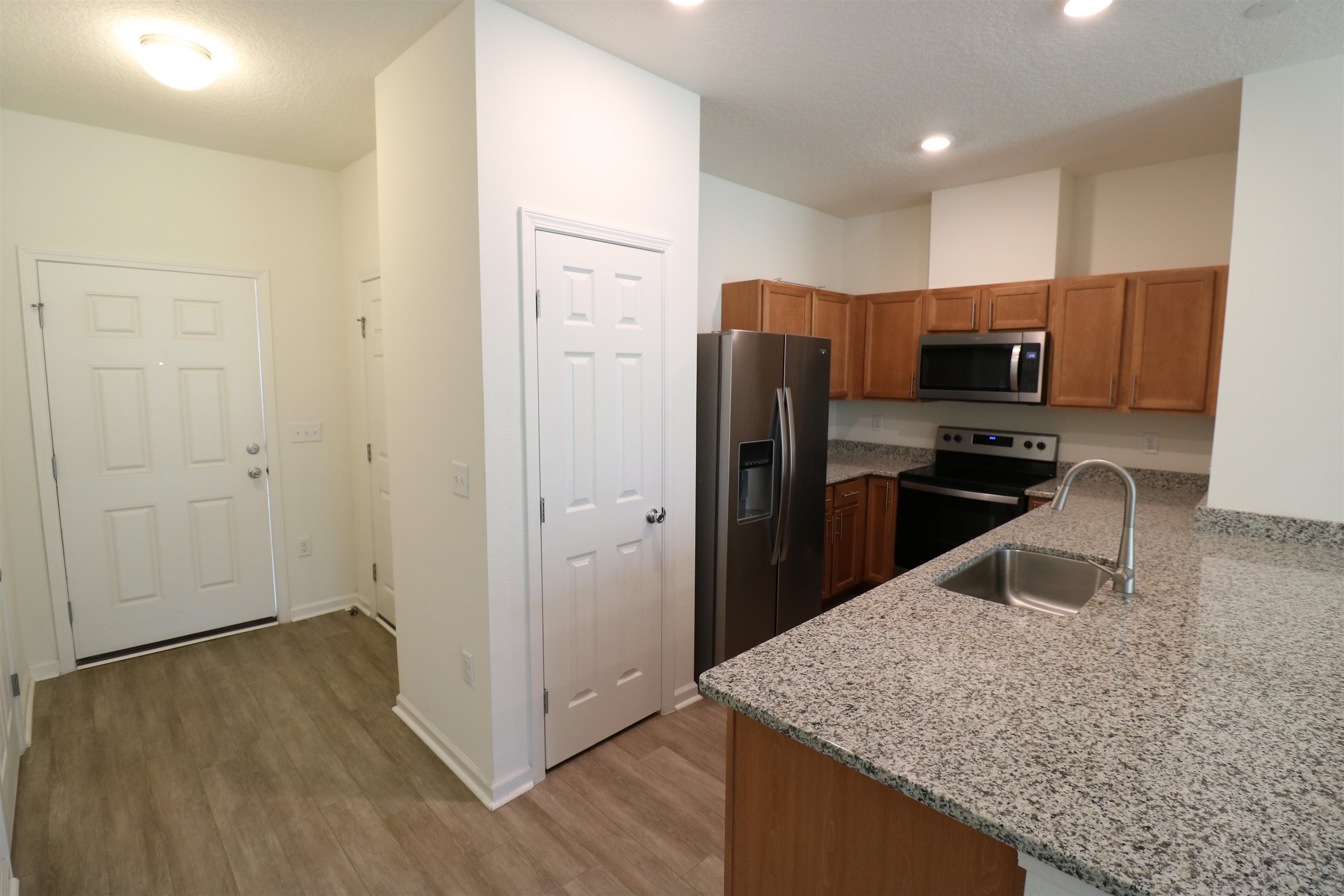 43 Mustard Hill St. Augustine, FL 32086 - Photo 3 of 25 Kitchen featuring light stone countertops, stainless steel appliances, wood finish cabinetry, light wood finished floors, and a textured ceiling