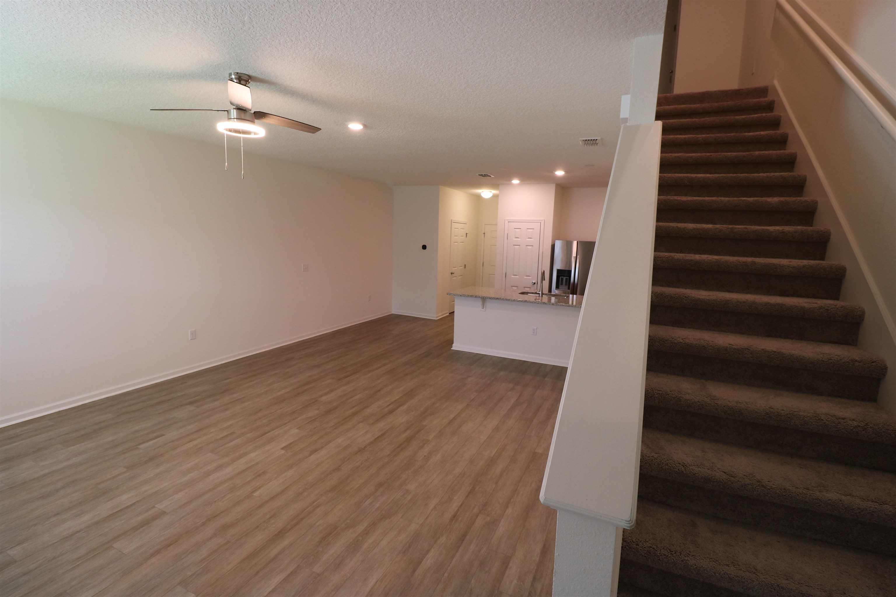 43 Mustard Hill St. Augustine, FL 32086 - Photo 6 of 25 Unfurnished living room featuring dark wood-type flooring, ceiling fan, a textured ceiling, and recessed lighting with carpet on the stairs.