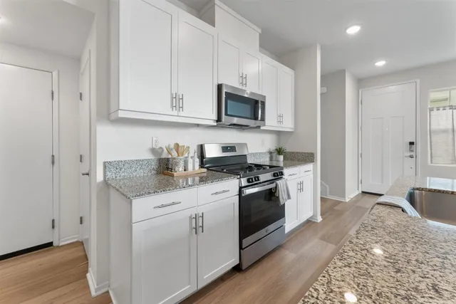 a kitchen with stainless steel appliances granite countertop white cabinets a sink a stove a refrigerator and microwave with wooden floor