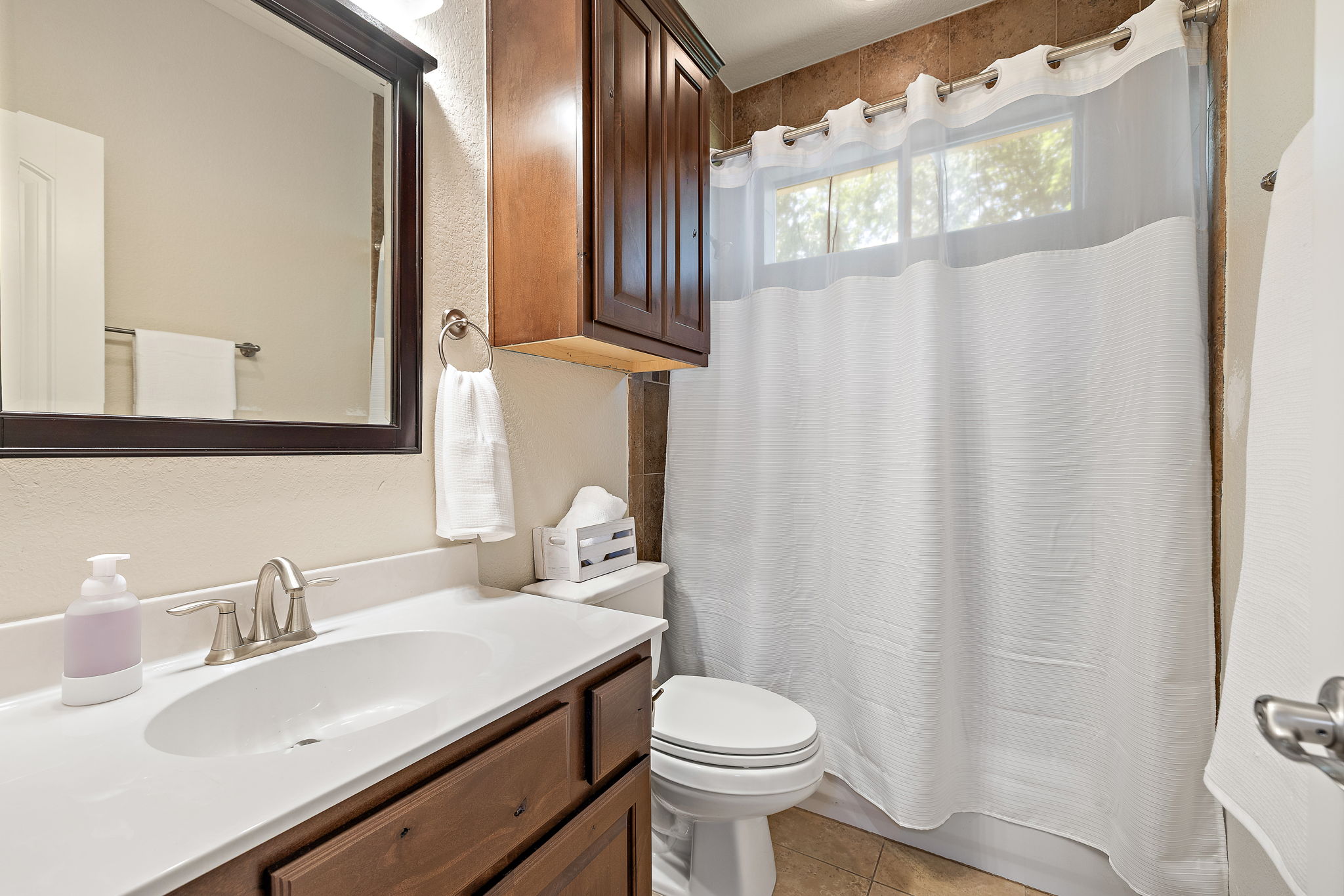 6708 Menchaca Road, Unit 10 Austin, TX 78745 - Photo 22 of 28 Bathroom featuring a vanity with a white countertop and wood-finish cabinetry, a framed mirror, a toilet, an upper storage cabinet, and a shower with brown tile surround