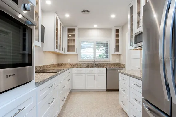 a large kitchen with stainless steel appliances granite countertop a refrigerator a sink dishwasher a oven and white cabinets with wooden floor