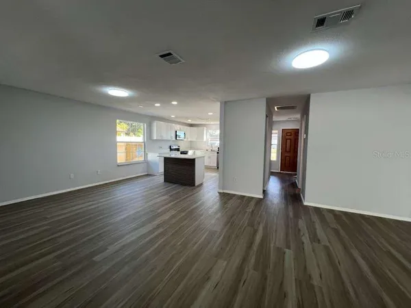 a view of empty room with wooden floor and kitchen view