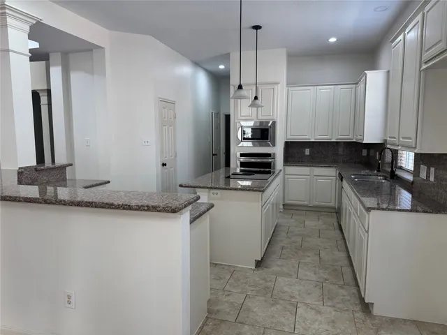 a large kitchen with granite countertop a sink and white cabinets