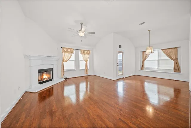 an empty room with wooden floor fireplace and windows