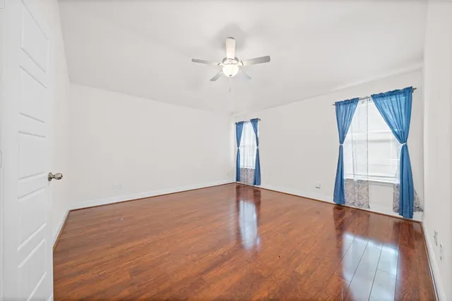 an empty room with wooden floor fan and windows