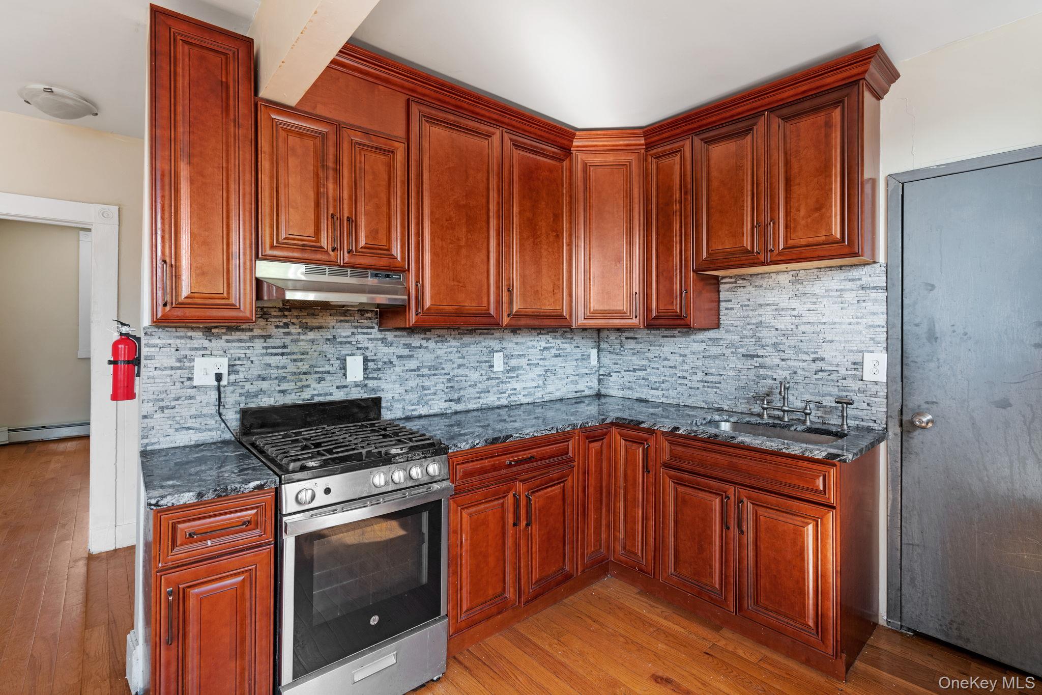 77 Academy Street Poughkeepsie, NY 12601 - Photo 15 of 30 Kitchen featuring stainless steel gas range oven, light wood finished floors, backsplash, under cabinet range hood, and dark stone counters