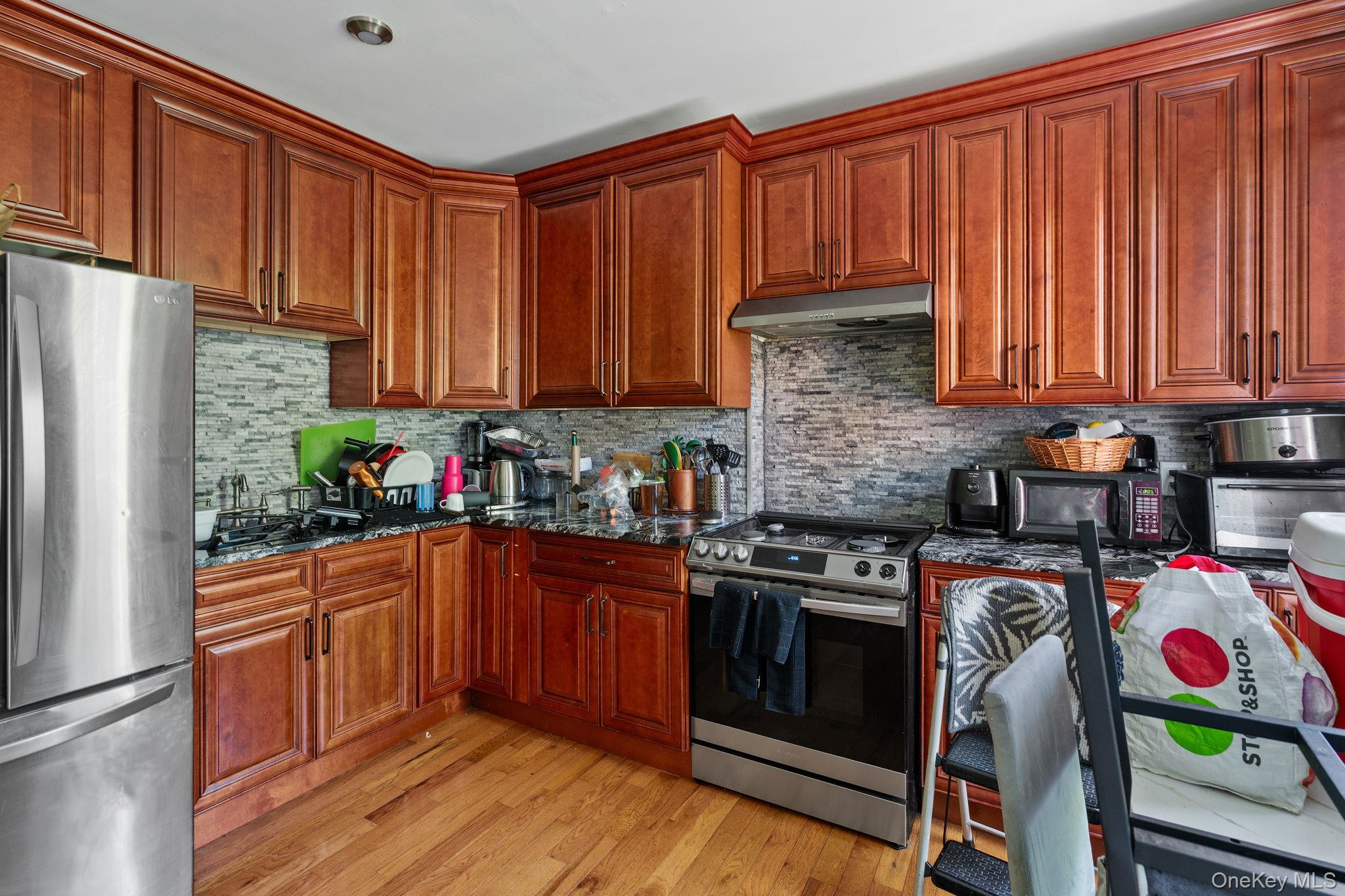 77 Academy Street Poughkeepsie, NY 12601 - Photo 22 of 30 Kitchen featuring stainless steel appliances, dark stone counters, light wood-type flooring, backsplash, and under cabinet range hood