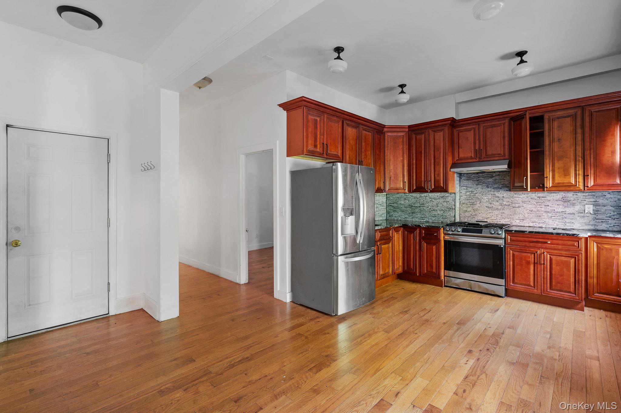 77 Academy Street Poughkeepsie, NY 12601 - Photo 6 of 30 Kitchen featuring appliances with stainless steel finishes, tasteful backsplash, light wood-style floors, dark stone countertops, and under cabinet range hood
