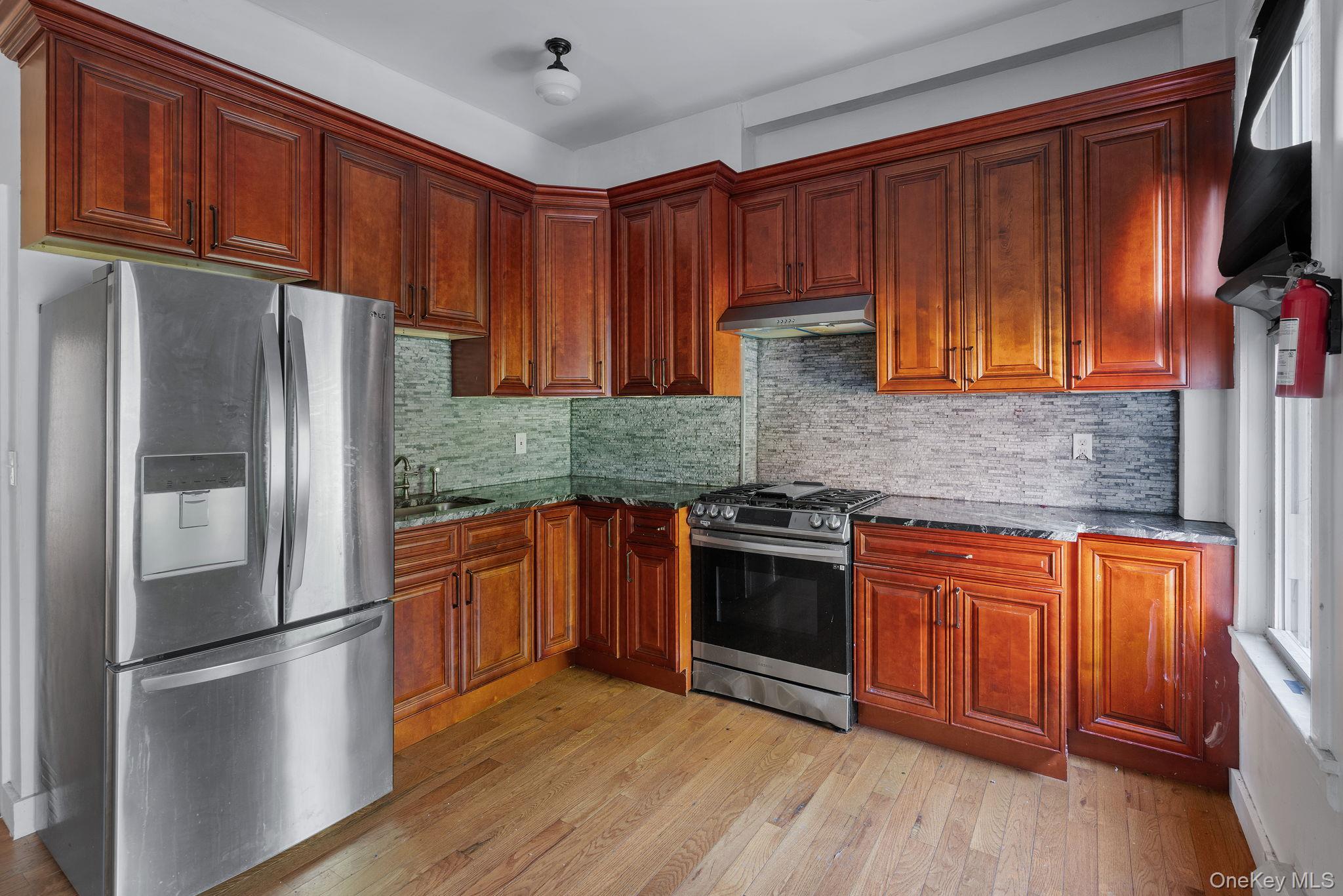 77 Academy Street Poughkeepsie, NY 12601 - Photo 7 of 30 Kitchen featuring stainless steel appliances, dark stone countertops, light wood-style floors, tasteful backsplash, and under cabinet range hood