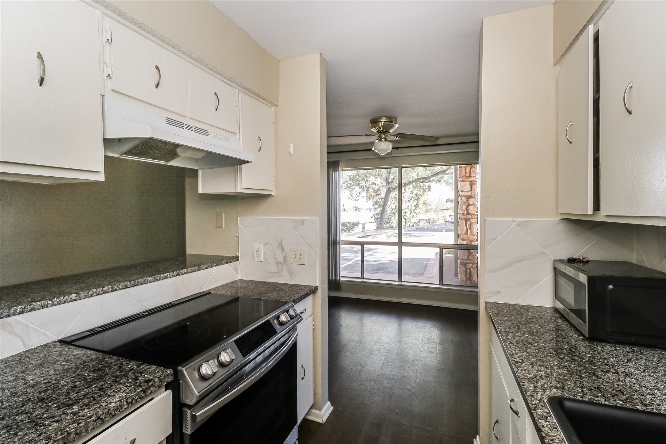 500 East Riverside Drive, Unit 135 Austin, TX 78704 - Photo 10 of 16 Kitchen with appliances with stainless steel finishes, a ceiling fan, under cabinet range hood, white cabinets, and dark stone countertops