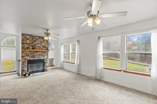 a view of a livingroom with a fireplace a ceiling fan and windows