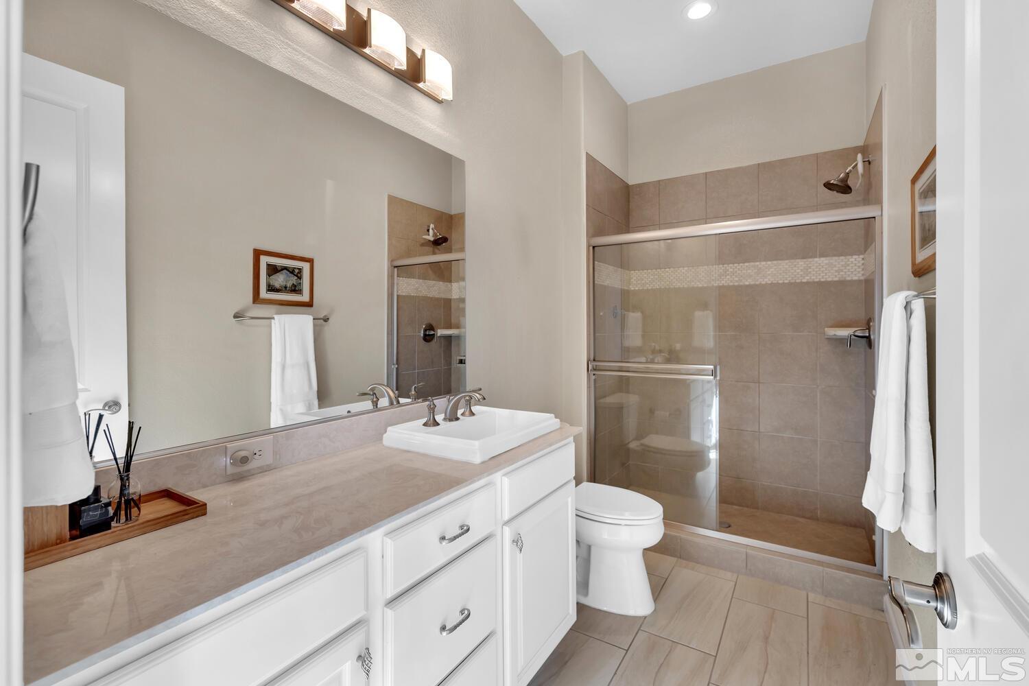 9775 Thesolious Lane Reno, NV 89521 - Photo 27 of 40 a bathroom with a granite countertop sink toilet a large mirror a shower and vanity