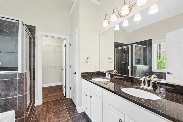 a spacious bathroom with a granite countertop double vanity sink a mirror and a shower