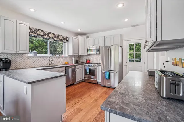 a kitchen with stainless steel appliances granite countertop a refrigerator a sink a stove and a refrigerator with wooden floor