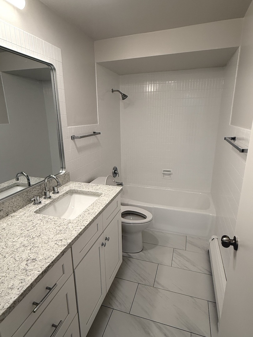 8304 W Forest, Unit 1W Chicago, IL 60634 - Photo 6 of 6 a bathroom with a granite countertop sink a toilet and bathtub