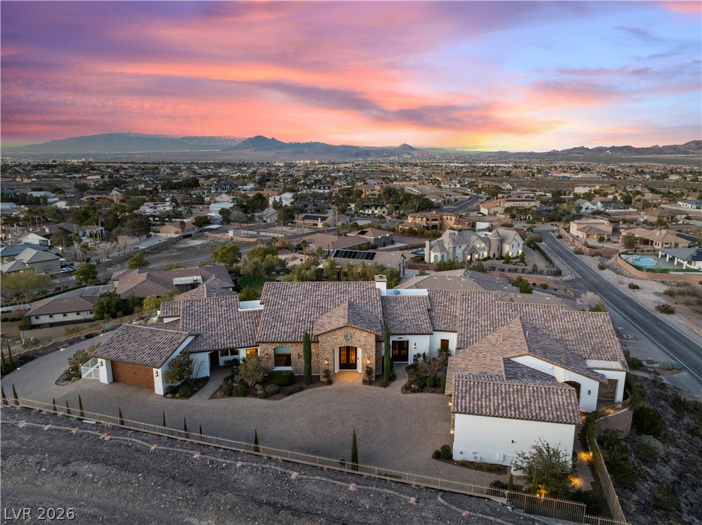 1123 Christian Road Henderson, NV 89002 - Photo 3 of 94 An aerial perspective reveals a magnificent home with tile roofing, nestled into a landscape with distant mountains under a striking sunset.